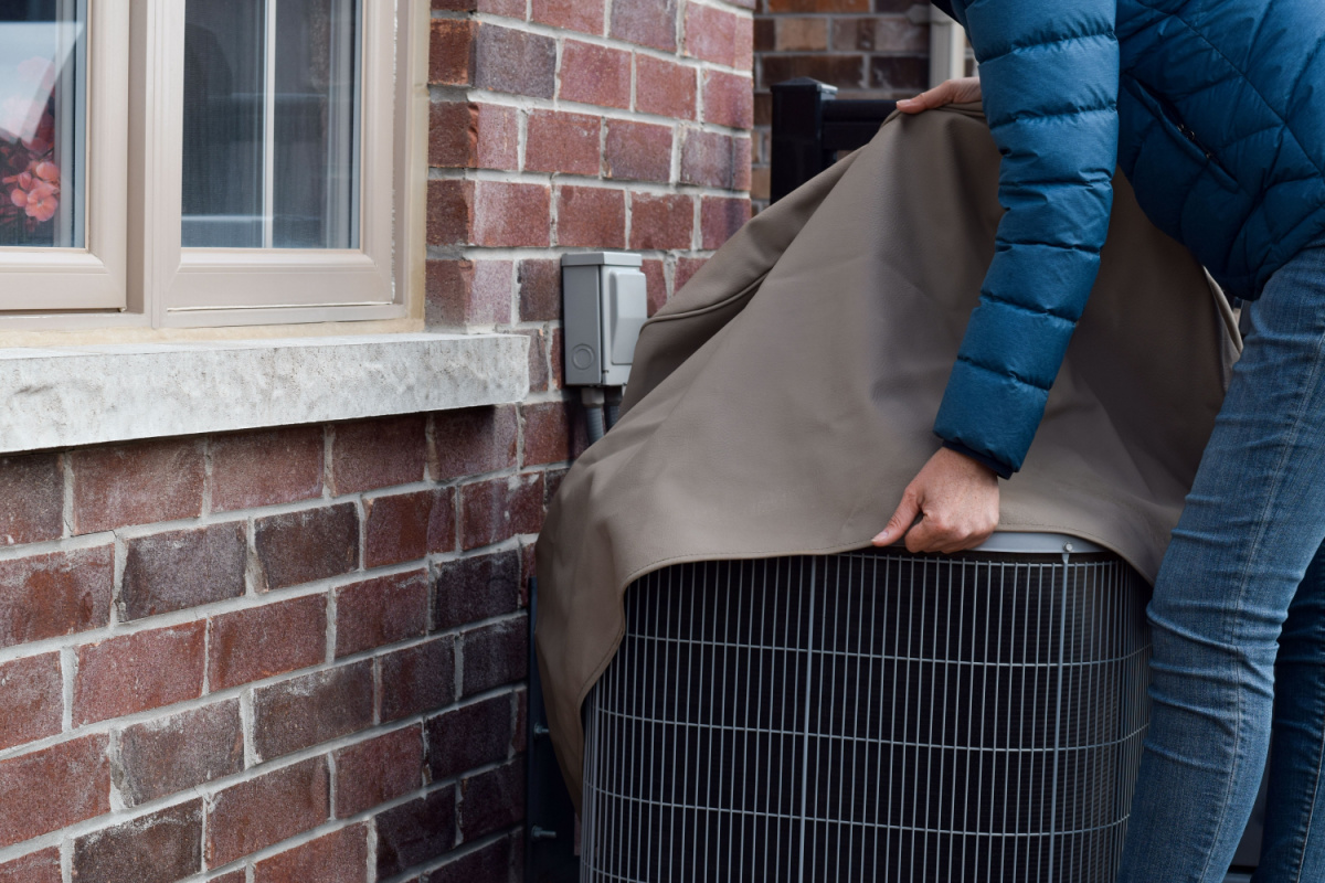 Homeowner winterizing their HVAC system by placing a cover over the condenser unit