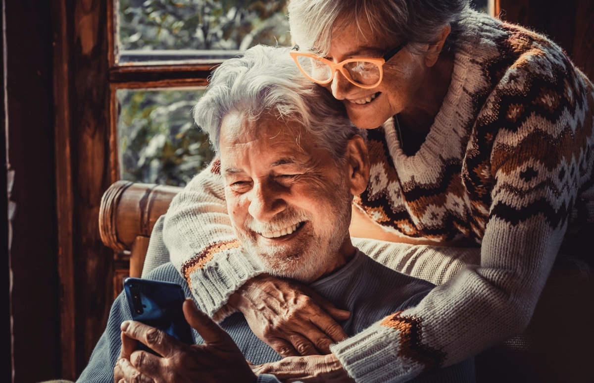 elderly couple hugging as they peruse new heating options on a cell phone