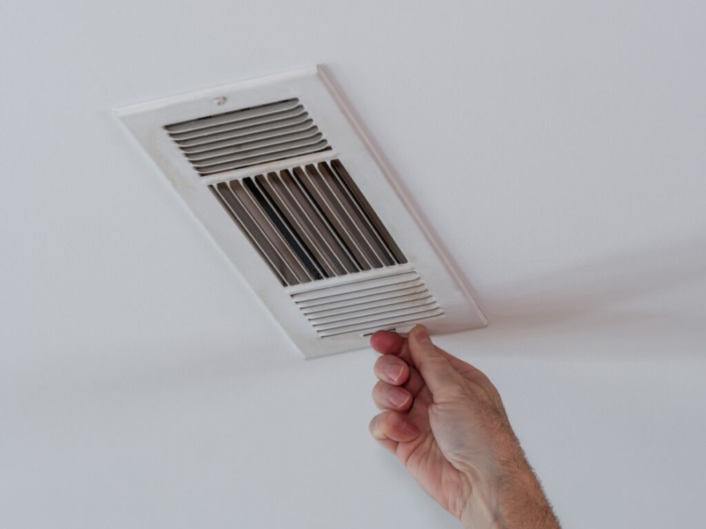 A man's hand reaching up toward an air vent to close it