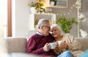 An older couple cuddling on the couch with cups of coffee