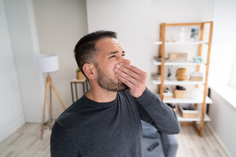 A man holding his nose in the living room because his furnace is producing a bad smell