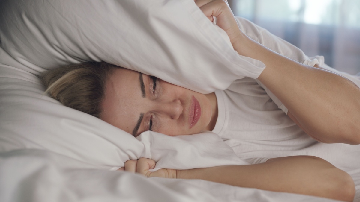 a woman lying in bed and covering her head with a pillow because her heating system is loud