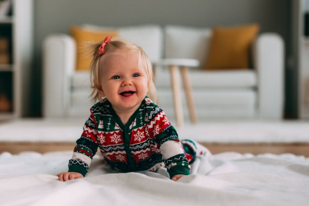 A happy girl baby crawling on the carpet wearing a Christmas-themed onesie