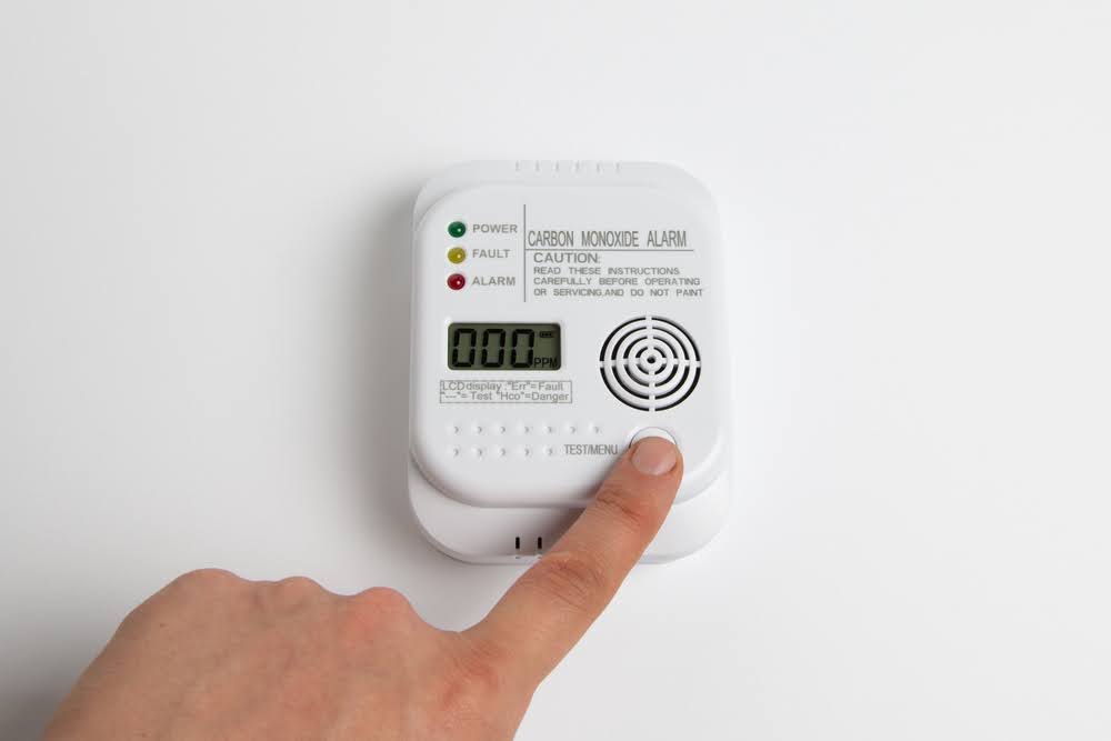 a hand testing a white carbon monoxide alarm installed on a home's wall