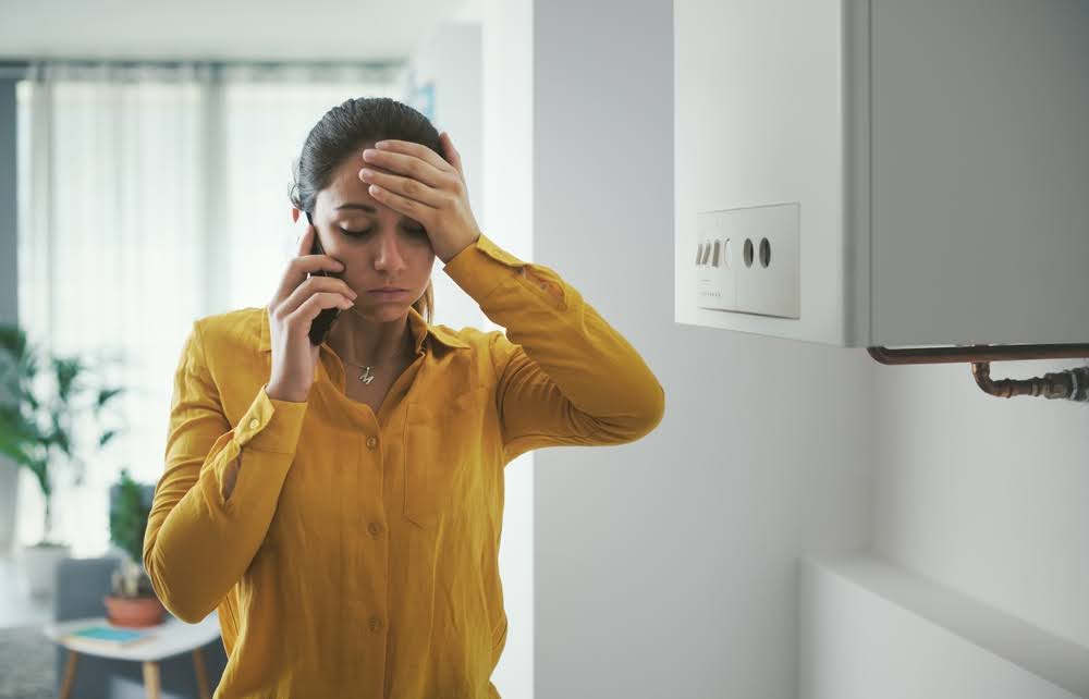 A stressed woman with her hand on her forehead as she's on the phone with a technician about her broken boiler