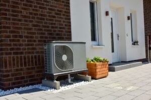 A dual-fuel heat pump installed outside a brick home next to the front door