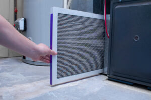 hand of a technician sliding a new furnace filter into the furnace unit