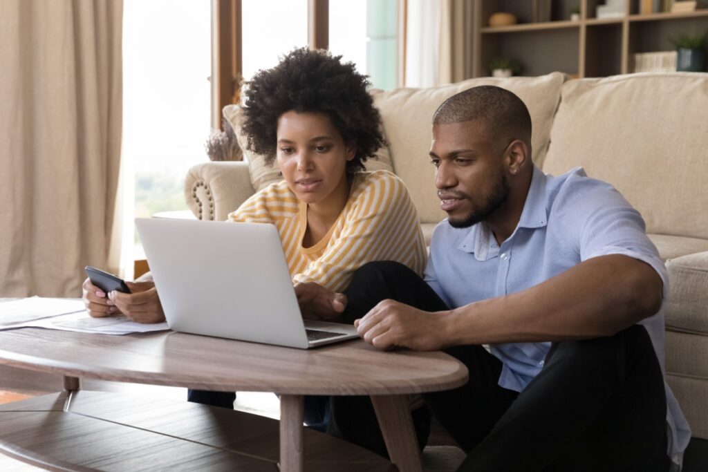 husband and wife sitting on the floor while researching furnaces vs. heat pumps on their laptop