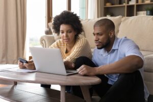 husband and wife sitting on the floor while researching furnaces vs. heat pumps on their laptop